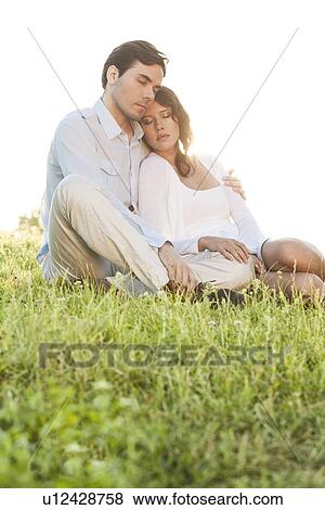 Relaxed couple with eyes closed sitting on grass in park View Large Photo Image Stock Photo - Relaxed couple with eyes closed sitting on grass in park. Fotosearch