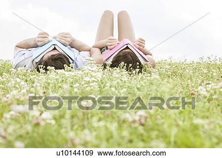Stock Photo - Relaxed young couple covering faces with books while lying on grass. Fotosearch