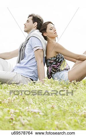 Relaxed young couple sitting back to back in park View Large Photo Image Picture - Relaxed young couple sitting back to back in park. Fotosearch