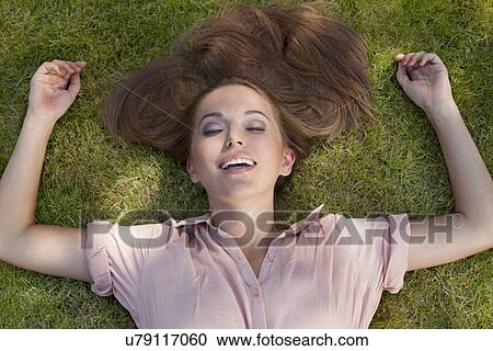 Relaxed young woman lying in grass at park View Large Photo Image Stock Image - Relaxed young woman lying in grass at park. Fotosearch