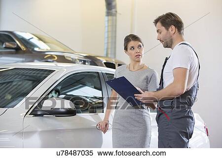 Stock Photography - Repairman holding clipboard while conversing with female customer in automobile repair shop. Fotosearch