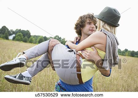 Stock Photo - Romantic man carrying woman in field. Fotosearch
