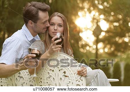 Stock Photo - Romantic young couple having red wine on chairs in park. Fotosearch
