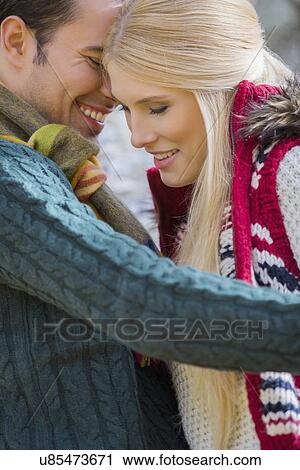 Stock Image - Romantic young couple in sweaters smiling at park. Fotosearch