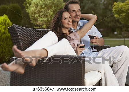 Stock Photo - Romantic young couple on easy chair looking away in park. Fotosearch