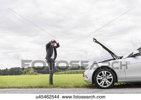 Picture - Sad young businessman standing with hands on head near broken car at countryside. Fotosearch