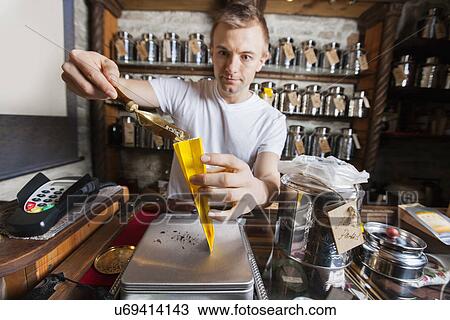 Stock Image - Salesperson scooping ingredient into paper bag at tea store. Fotosearch