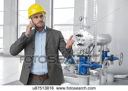 Serious young male manager using cell phone in industry View Large Photo Image Stock Photograph - Serious young male manager using cell phone in industry. Fotosearch