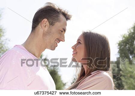 Stock Photo - Side view of affectionate young couple looking at each other in park. Fotosearch