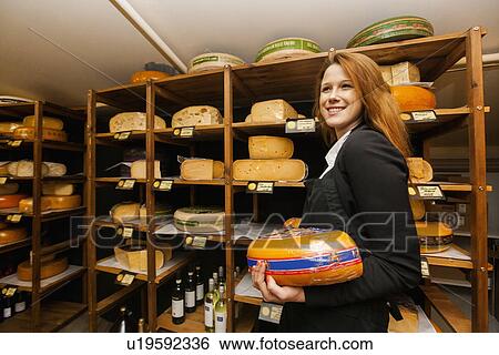 Stock Photograph - Side view of female salesperson holding cheese in store. Fotosearch