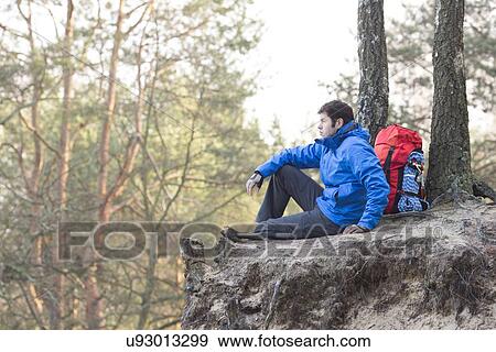 Side view of hiker sitting on edge of cliff in forest View Large Photo Image Stock Photo - Side view of hiker sitting on edge of cliff in forest. Fotosearch