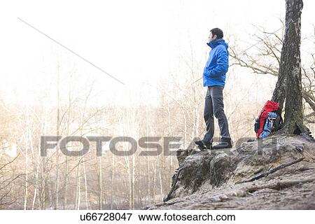 Stock Photo - Side view of hiker standing on edge of cliff in forest. Fotosearch