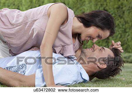 Stock Image - Side view of loving woman lying on man in park. Fotosearch