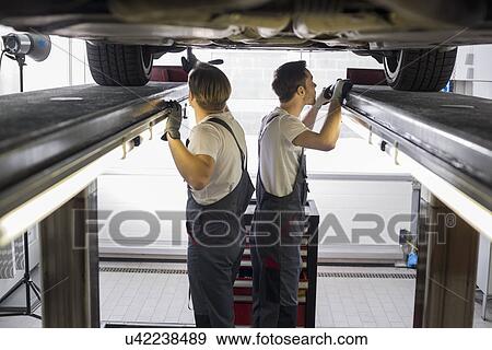 Stock Photo - Side view of maintenance engineers examining car in repair shop. Fotosearch
