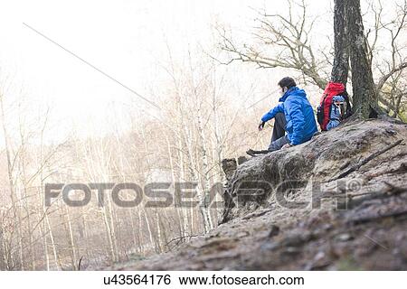 Side view of male hiker sitting on edge of cliff in forest View Large Photo Image Stock Photograph - Side view of male hiker sitting on edge of cliff in forest. Fotosearch