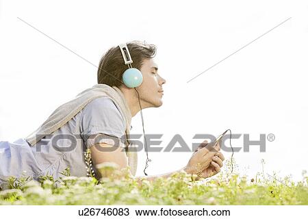 Stock Image - Side view of man enjoying music on MP3 player using headphones in park against clear sky. Fotosearch
