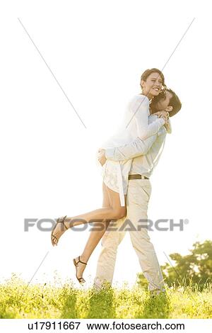 Stock Photo - Side view of man lifting woman in park against clear sky. Fotosearch