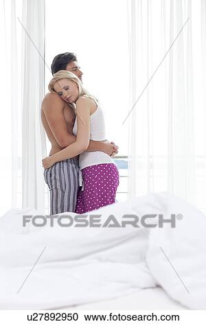 Side view of relaxed young couple hugging in bedroom View Large Photo Image Stock Image - Side view of relaxed young couple hugging in bedroom. Fotosearch