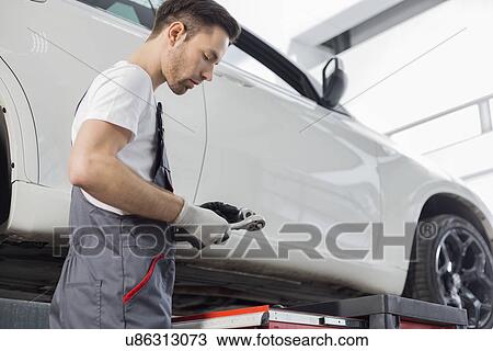 Side view of repairman holding tool while standing by car in workshop View Large Photo Image Stock Image - Side view of repairman holding tool while standing by car in workshop. Fotosearch