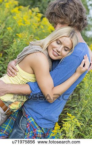 Stock Photograph - Side view of romantic couple hugging in field. Fotosearch