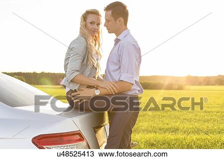 Stock Image - Side view of romantic young couple by car at countryside. Fotosearch