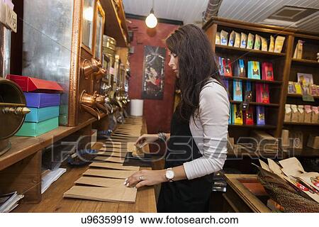 Stock Photo - Side view of salesperson stamping paper bags at coffee store. Fotosearch