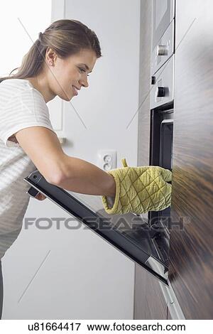 Side view of smiling woman placing dish in oven View Large Photo Image Stock Photo - Side view of smiling woman placing dish in oven. Fotosearch