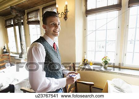 Stock Image - Side view of waiter with notepad smiling in restaurant. Fotosearch