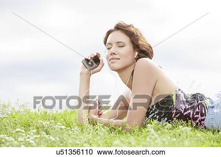 Side view of woman listening to music through MP3 player using headphones while lying on grass against sky View Large Photo Image Stock Image - Side view of woman listening to music through MP3 player using headphones while lying on grass against sky. Fotosearch