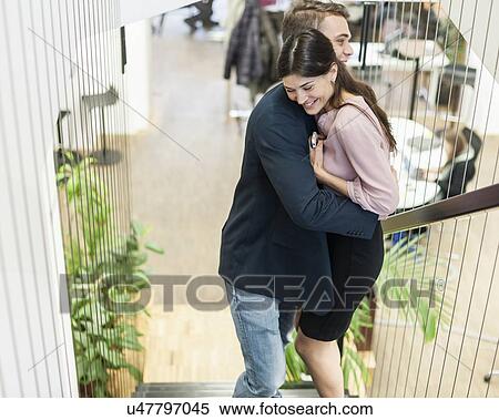 Stock Photography - Side view of young business couple hugging on staircase. Fotosearch