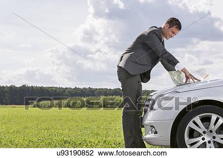 Side view of young businessman looking at map on car hood at countryside View Large Photo Image Stock Image - Side view of young businessman looking at map on car hood at countryside. Fotosearch