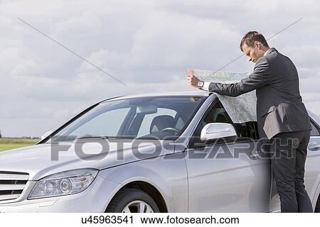 Side view of young businessman reading map by car at countryside View Large Photo Image Stock Image - Side view of young businessman reading map by car at countryside. Fotosearch