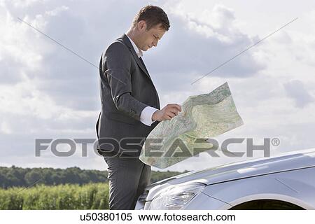 Side view of young businessman reading map by car at countryside View Large Photo Image Stock Photography - Side view of young businessman reading map by car at countryside. Fotosearch