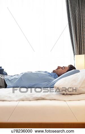 Side view of young businessman sleeping on bed in hotel room View Large Photo Image Stock Image - Side view of young businessman sleeping on bed in hotel room. Fotosearch