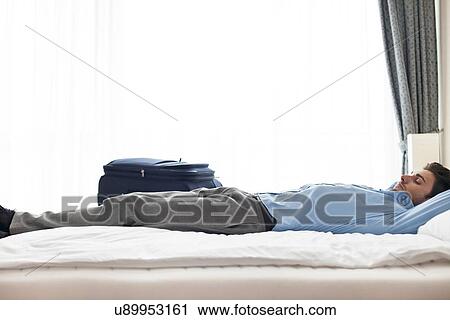 Stock Image - Side view of young businessman sleeping in hotel room. Fotosearch