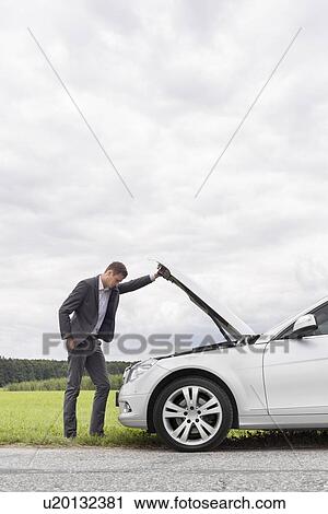 Side view of young businessman examining broken down car engine at countryside View Large Photo Image Stock Image - Side view of young businessman examining broken down car engine at countryside. Fotosearch