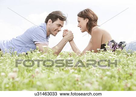 Side view of young couple arm wrestling while lying on grass against sky View Large Photo Image Stock Image - Side view of young couple arm wrestling while lying on grass against sky. Fotosearch