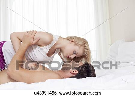 Stock Photograph - Side view of young couple cuddling in bed. Fotosearch