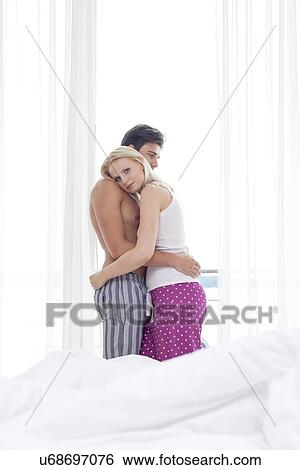 Stock Photograph - Side view of young couple hugging in hotel room. Fotosearch