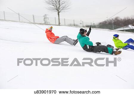 Stock Image - Side view of young friends sledging on snow covered slope. Fotosearch