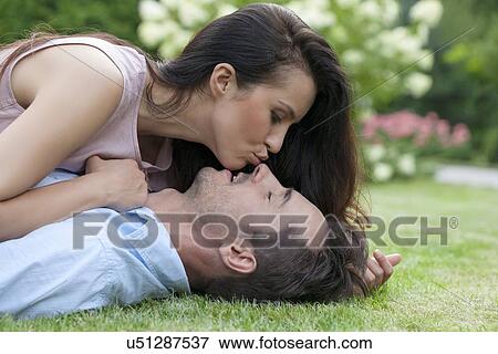 Side view of young woman kissing man while lying in park View Large Photo Image Stock Photo - Side view of young woman kissing man while lying in park. Fotosearch