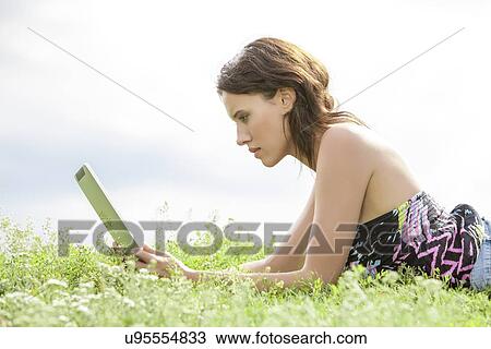 Side view of young woman using Tablet PC while lying on grass against sky View Large Photo Image Stock Image - Side view of young woman using Tablet PC while lying on grass against sky. Fotosearch