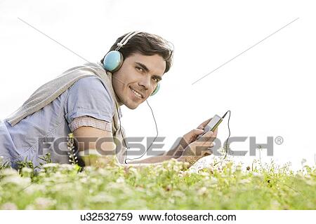 Stock Photo - Side view portrait of man listening to music on MP3 player using headphones in park against clear sky. Fotosearch