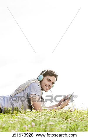 Side view portrait of man listening to music on MP3 player using headphones in park against clear sky View Large Photo Image Stock Photo - Side view portrait of man listening to music on MP3 player using headphones in park against clear sky. Fotosearch