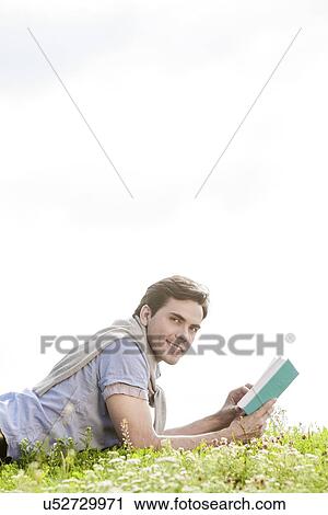 Side view portrait of young man holding book while lying on grass against clear sky View Large Photo Image Stock Image - Side view portrait of young man holding book while lying on grass against clear sky. Fotosearch