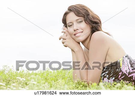 Picture - Side view portrait of young woman lying on grass against clear sky. Fotosearch