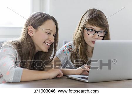 Stock Photograph - Sisters using laptop together at home. Fotosearch