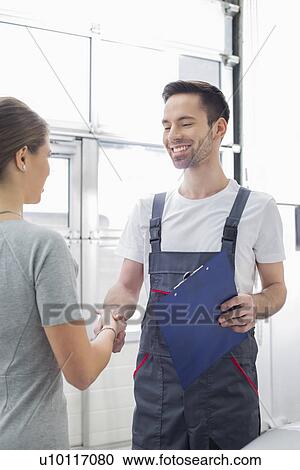 Stock Image - Smiling automobile mechanic shaking hands with female customer in automobile repair shop. Fotosearch