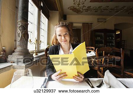 Stock Photo - Smiling customer holding menu at restaurant table. Fotosearch