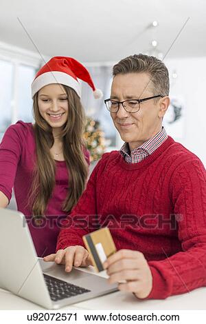 Stock Image - Smiling father and daughter shopping online at home during Christmas. Fotosearch